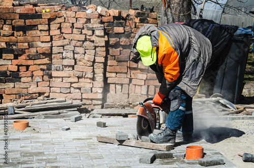 A worker cuts paving slabs with a gas cutter and a hand saw