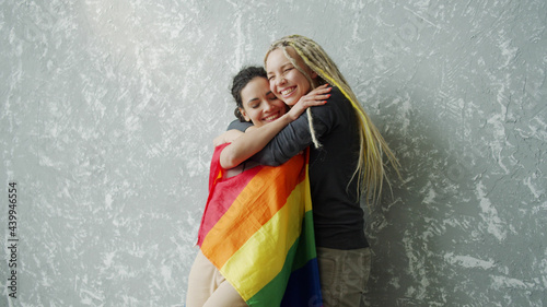 Covered with LGBTQ flag girl tenderly hugs her girlfriend