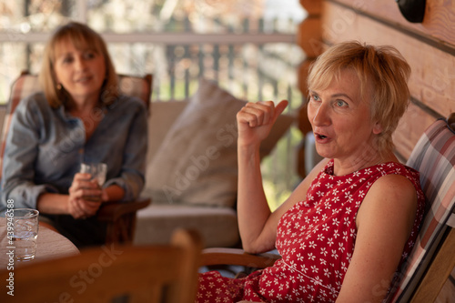 Lifestyle photo of two women sisters 55 years old, patio wooden house © Татьяна Волкова