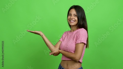 Young woman extending hands to the side and inviting to come over isolated background. Green screen chroma key