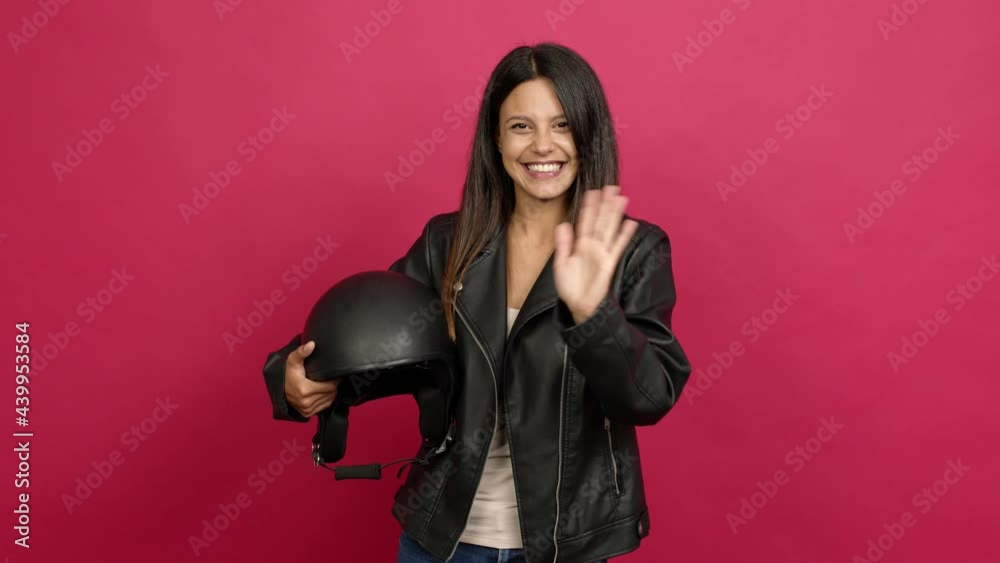 Young woman holding a motorcycle helmet saluting with hand with happy expression over isolated background