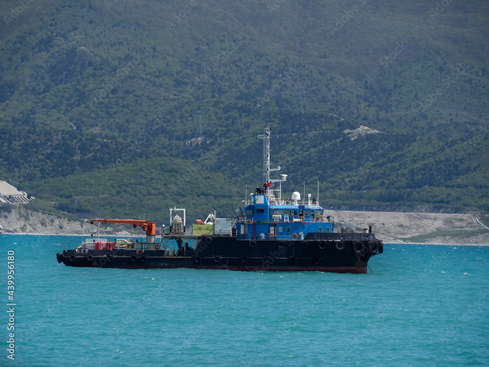 Port tug with a crane in the Tsemesskaya bay of the Black Sea. Towboat on the background of the mountains.