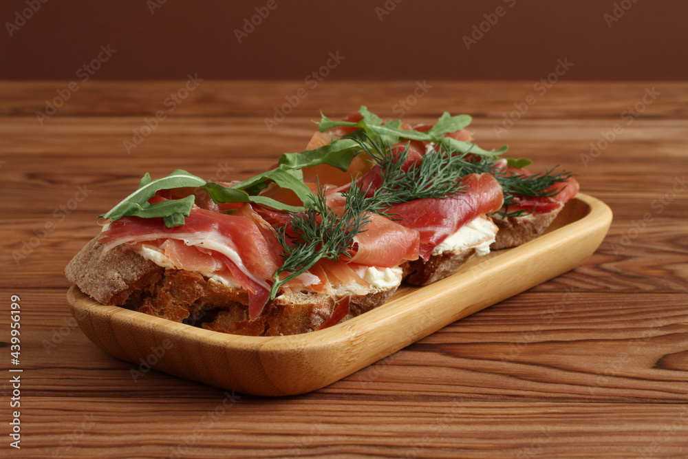 Buckwheat toasts with goat cheese, ham and arugula lying on a bamboo plate on a wooden table. Closeup