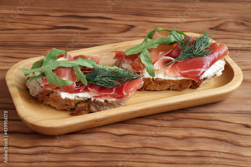 Buckwheat toasts with goat cheese, ham and arugula lying on a bamboo plate on a wooden table. Closeup