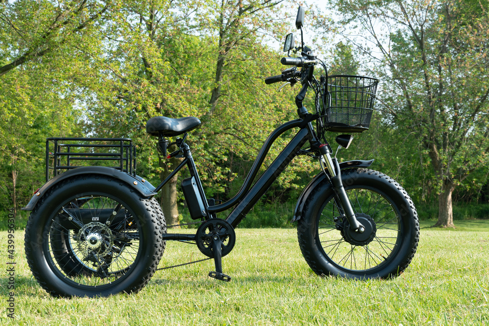 Electric trike or e bicycle in the park in sunny summer day. Shot from the side. A lot of lighting. The view of the e motor and power battery of the three wheel bike.