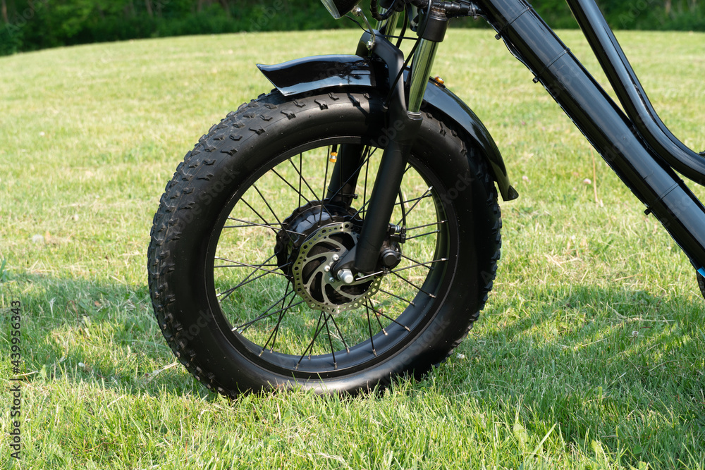 Wheel of the electric bicycle view from side. E bike motor in the park grass of the city. Unfiltered, with natural lighting, urban view. Ecology and green energy concept. Ev – electric vehicle. Wheel of the electric bicycle view from side. E bike motor in the park grass of the city. Unfiltered, with natural lighting, urban view. Ecology and green energy concept. Ev – electric vehicle.