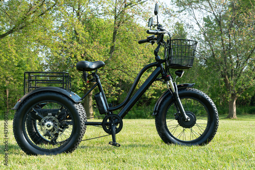 Electric trike or e bicycle in the park in sunny summer day. Shot from the side. A lot of lighting. The view of the e motor and power battery of the three wheel bike.