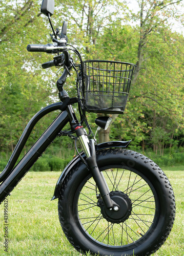 Front wheel side of the electric bicycle, view in sunny summer day in the green grass. E bike motor with battery. Ecology and green energy concept. Ev – electric vehicle.