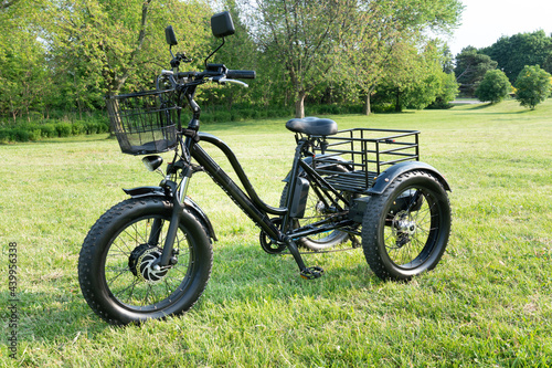 Front wheel side of the electric bicycle, view in sunny summer day in the green grass. E bike motor with battery. Ecology and green energy concept. Ev – electric vehicle.