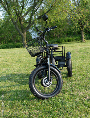 Front wheel side of the electric bicycle, view in sunny summer day in the green grass. E bike motor with battery. Ecology and green energy concept. Ev – electric vehicle.