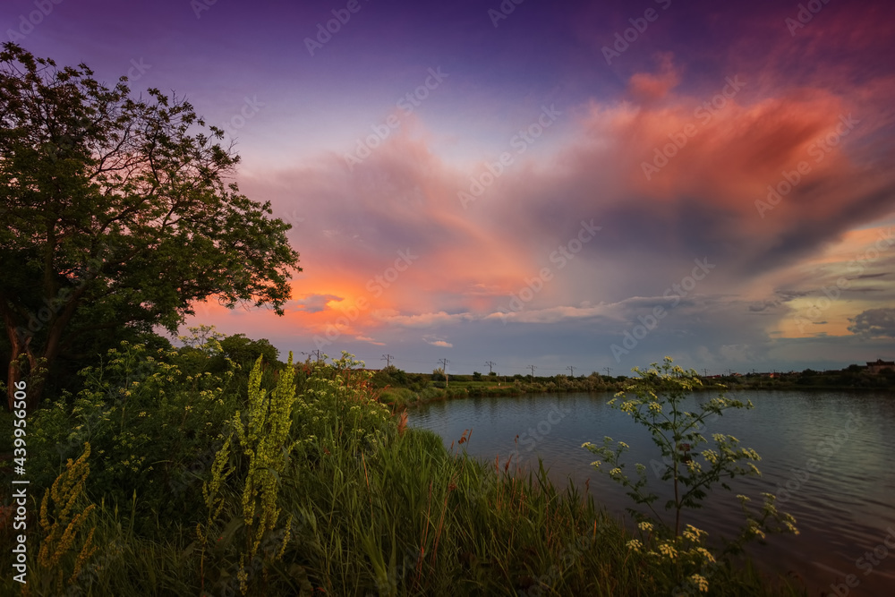 Amazing sunrise by the lake with colorful clouds and vegetation in the foreground