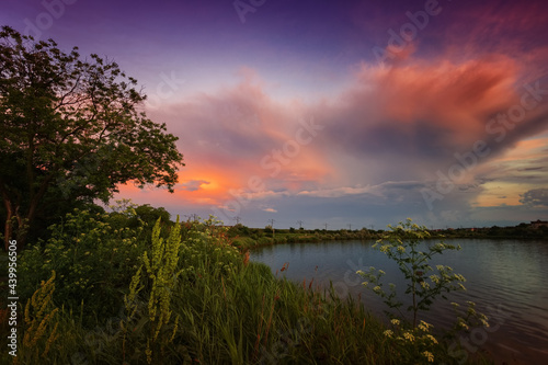 Amazing sunrise by the lake with colorful clouds and vegetation in the foreground