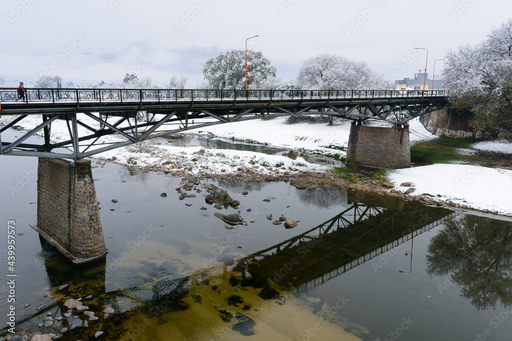 Obraz premium Reflejo del puente viejo sobre el río Cosquín en un día de nieve