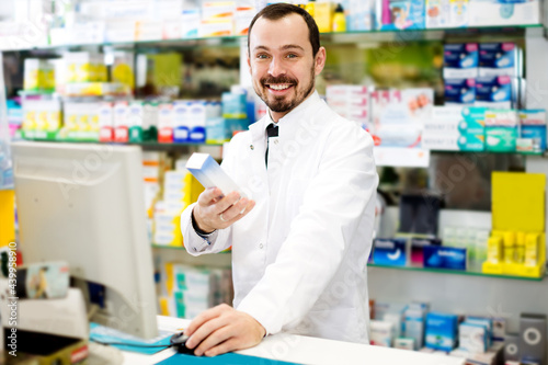 Happy male pharmacist checking assortment of drugs in pharmacy