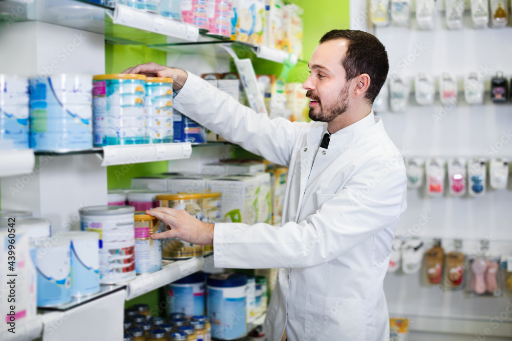 Cheerful positive male pharmacist looking for right medicine in pharmacy