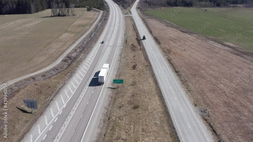 Drone shot rising over highway next to country road in Sweden with car, truck and tractor driving. Drone shot rising over highway next to country road in Sweden with car, truck and tractor driving.