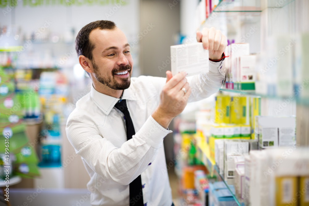 Positive man customer looking rows of pills in drugstore