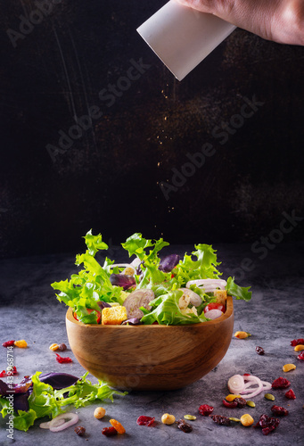 hand holds pepper shaker and sprinkles salad