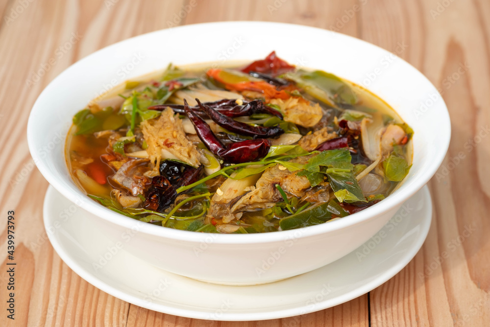 Sour and Spicy Smoked Dry Fish Soup in a white ceramic plate on a wooden table . Tom Klong IN Thai. Thai Food. Sour and Spicy Smoked Dry Fish Soup in a white ceramic plate on a wooden table . Tom Klong IN Thai. Thai Food.