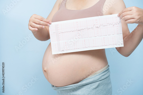 Close up Pregnant woman holding ctg graph in hand on blue background. Waiting baby concept. photo