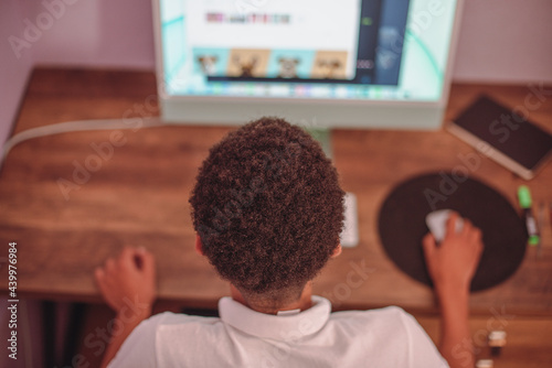 Rear view of young boy using his computer at home