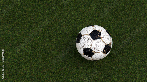 Top down view above old Soccer or football ball with paint peeling off on artificial green grass background with copy or negative space
