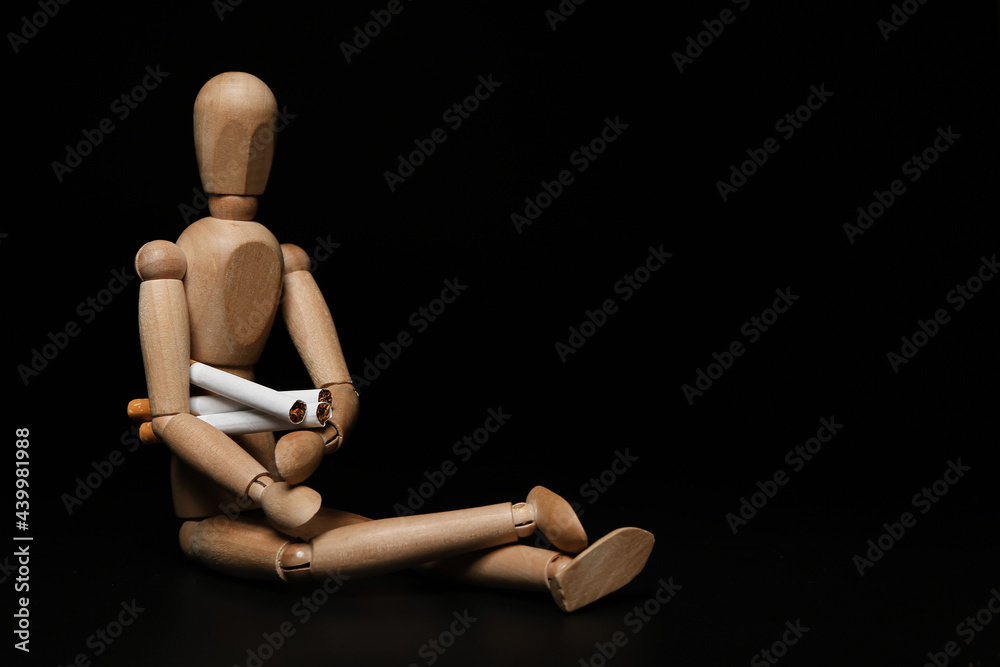 Wooden human figurine with cigarettes on dark background Wooden human figurine with cigarettes on dark background