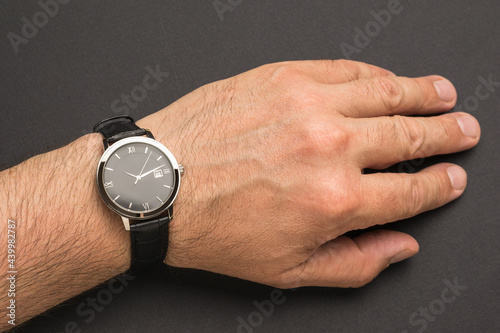 Men's hand with a classic wrist watch on a black background.