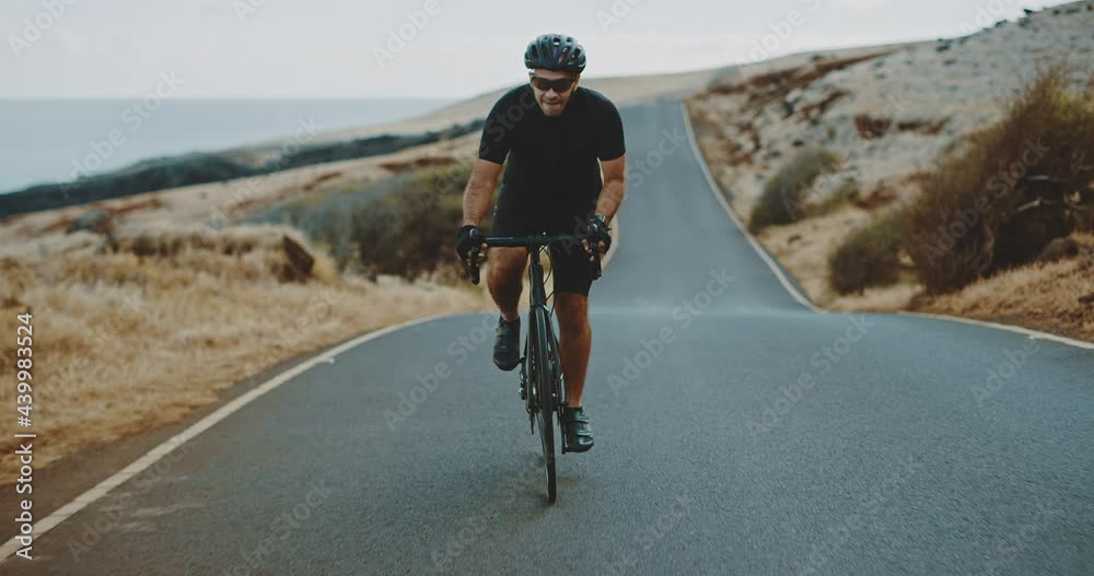 Road biker cycling up a steep hill on beautiful country road, exercise and fitness concept, healthy active lifestyle