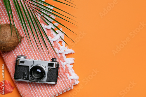 Towel, photo camera, coconut and palm leaf on color background