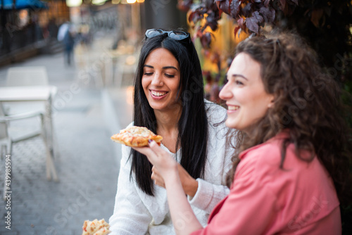 two girls eating pizza in the city two friends sitting eating. Two tourist on the street eating. A lesbian couple eating together