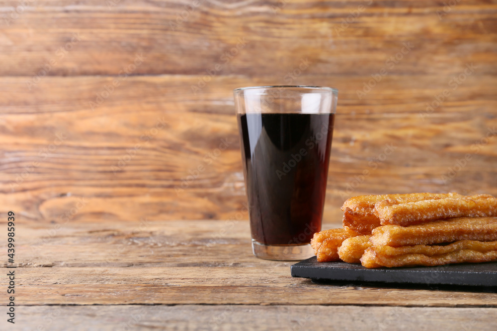 Board with tasty churros and glass of cola on wooden background Board with tasty churros and glass of cola on wooden background