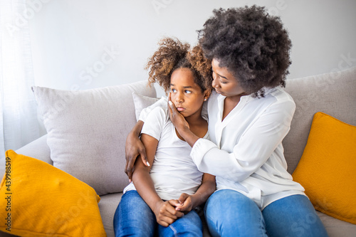 Focus on upset sad small daughter sitting on sofa with mother, mom scold kid for bad behaviour, child psychologist help girl deal with emotional social behavior problems trauma therapy support concept