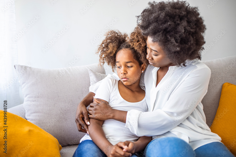 Black African mother embrace little preschool frustrated kid sitting on couch together at home. American loving mother supports disappointed daughter sympathizing, making peace after scolding concept Black African mother embrace little preschool frustrated kid sitting on couch together at home. American loving mother supports disappointed daughter sympathizing, making peace after scolding concept