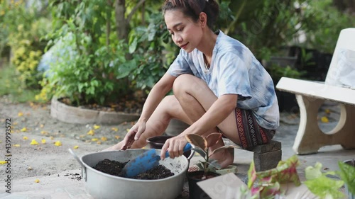 A young woman shovels soil into pots in preparation for happily planting a small plant at her home.