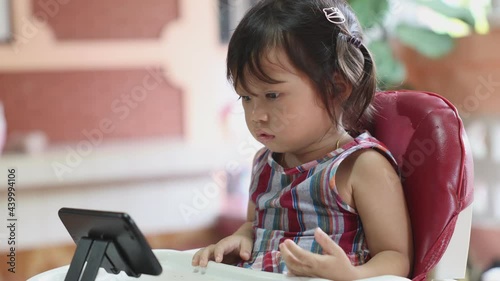 Asian girl sitting intently staring at the smartphone at the dining table, child addicted to phone concept, slide view