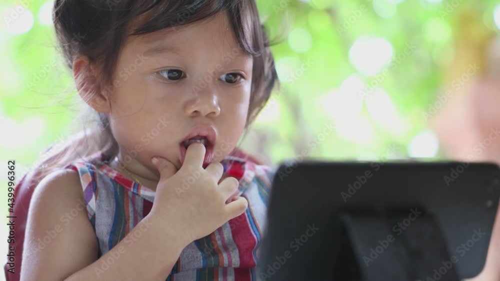 Asian girl sitting intently staring at a smartphone at the dining table and holding her hand, child addicted to distracted phone concept, front view Asian girl sitting intently staring at a smartphone at the dining table and holding her hand, child addicted to distracted phone concept, front view