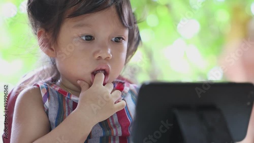 Asian girl sitting intently staring at a smartphone at the dining table and holding her hand, child addicted to distracted phone concept, front view