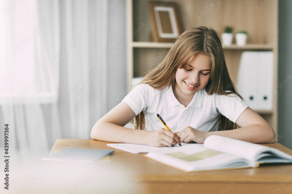 A smiling girl does her homework, writes a synopsis, and prepares for lectures. The concept of training and education A smiling girl does her homework, writes a synopsis, and prepares for lectures. The concept of training and education
