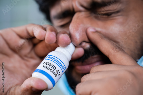 Extreme close up of Young man with medical face mask inhales coronavirus covid-19 nasal vaccination spray to protect from virus infection photo