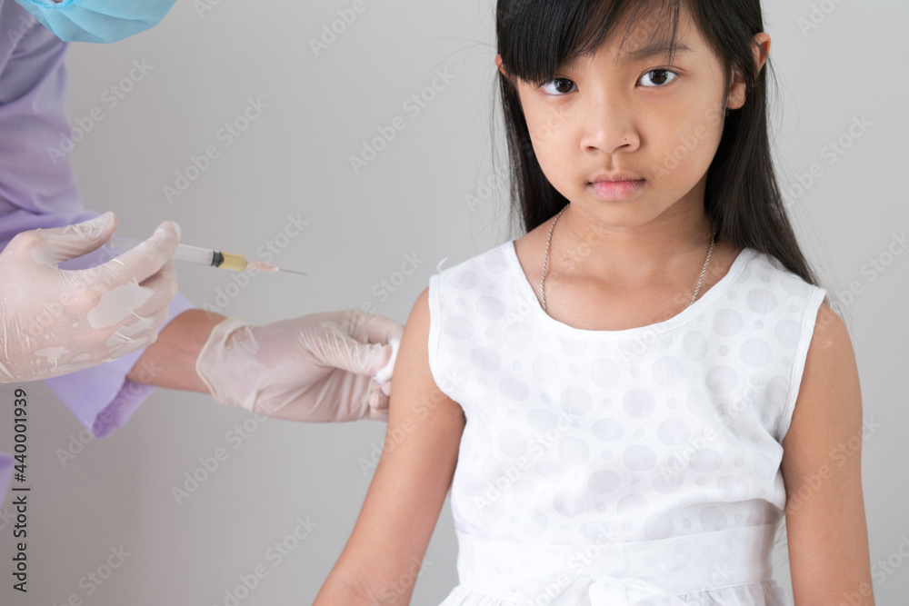 Female doctor or public health worker is injecting a flu treatment or a coronavirus or COVID-19 vaccine into the arm of an Asian child girl. Female doctor or public health worker is injecting a flu treatment or a coronavirus or COVID-19 vaccine into the arm of an Asian child girl.