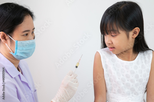 Female doctor or public health worker is injecting a flu treatment or a coronavirus or COVID-19 vaccine into the arm of an Asian child girl.