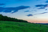 Evening twilight over the meadow. Bright dramatic sky and green grass. Rural landscape under a picturesque colorful sky at sunset.