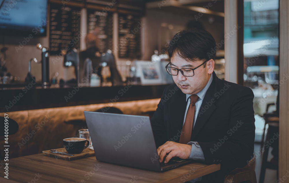 Fototapeta premium Asian businessman wearing suite and eyeglasses drink coffee , typing notebook for work at cafe restaurant. 