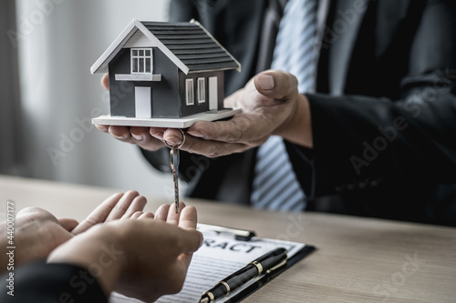 The salesperson handed the small gray model of the house and the house keys to the customer as a sign of home delivery after the contract was signed and the home inspected. Real estate concept.