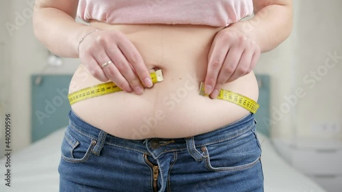 Young fat woman with excess weight measuring her big belly with measuring tape. Concept of dieting, unhealthy lifestyle, overweight and obesity