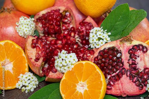Close-up of Cut Open Pomegranates and Oranges on a Wooden Table Outside with White Flowers