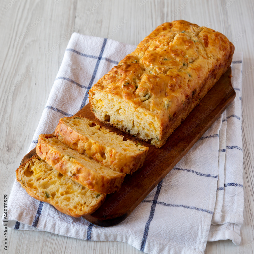 Homemade Cheesy Bread Loaf on a rustic wooden board on a white wooden background, side view. Homemade Cheesy Bread Loaf on a rustic wooden board on a white wooden background, side view.
