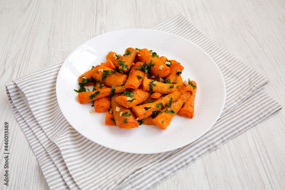Homemade Roasted Carrots with Herbs on a white plate on a white wooden background, side view. Homemade Roasted Carrots with Herbs on a white plate on a white wooden background, side view.