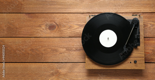 Turntable with vinyl record on wooden background, top view. Space for text